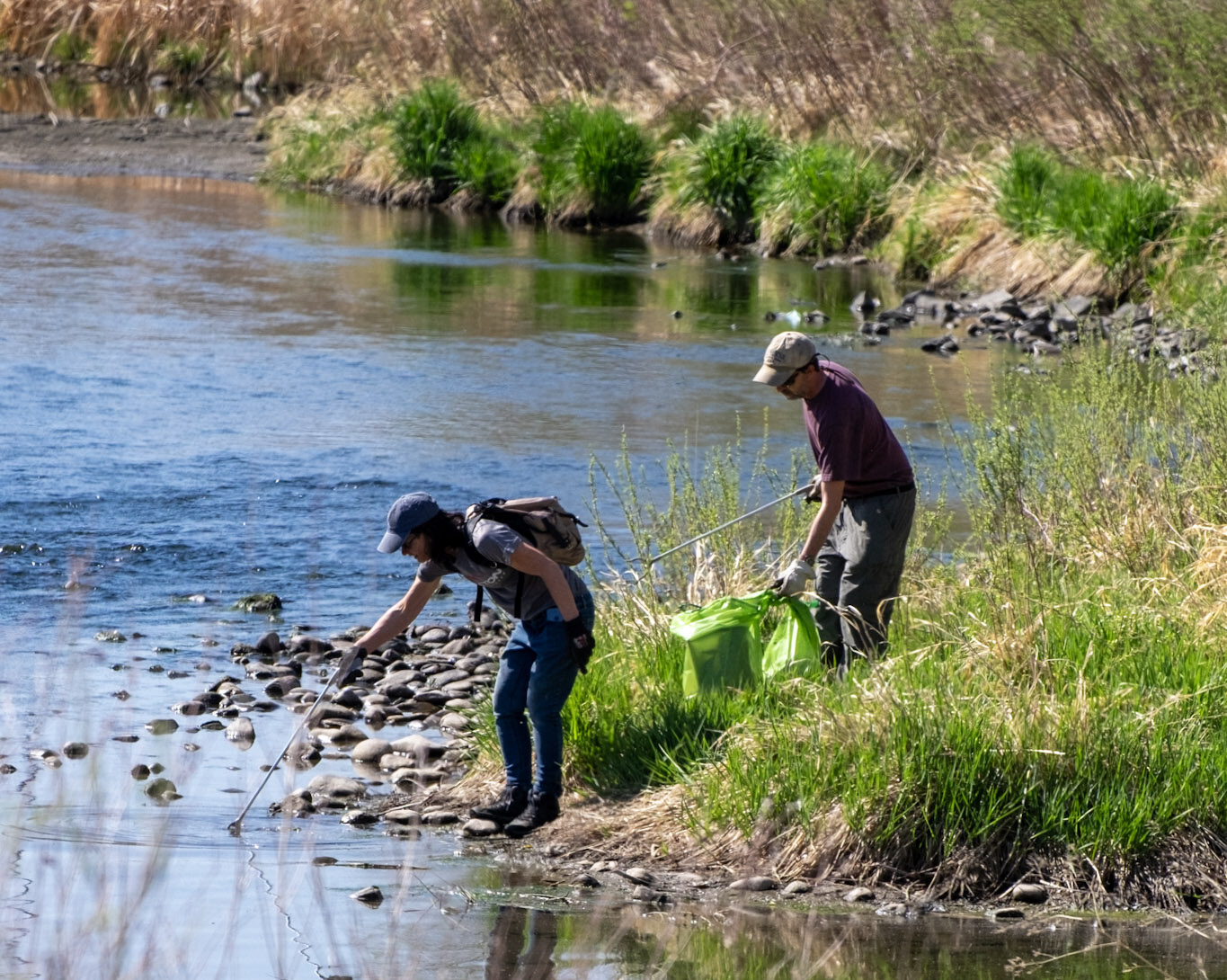 Two community members using pickers in river to pick up trash